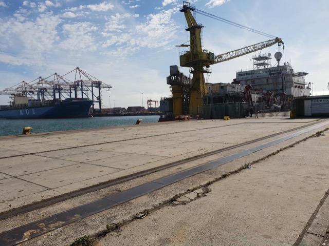 Ship-repair crane and vessel beyond a bare concrete quay apron